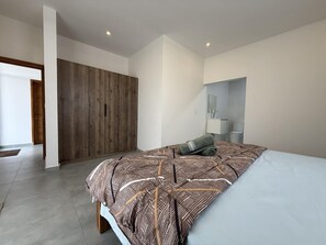 A modern bedroom with a large bed, a wardrobe, a bathroom with a mirror, and a door leading to another room. - Cozy Luxe - 4 bedrooms Villa with private pool (Mahebourg)