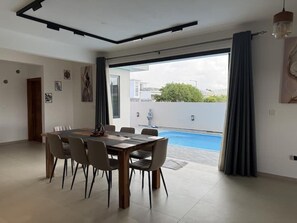 A modern living room with a dining table, chairs, a pool, and a large sliding glass door. - Cozy Luxe - 4 bedrooms Villa with private pool (Mahebourg)