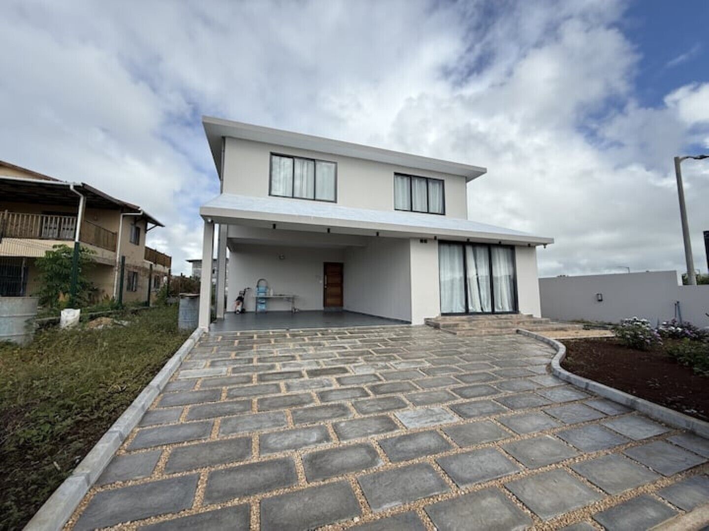 Une maison moderne à deux étages, dotée d’un patio couvert et d’une allée pavée.
