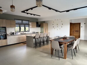 Uma cozinha moderna com uma ilha central, banquetas, uma mesa de jantar com cadeiras e uma porta de madeira.