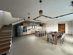 Eine moderne Küche mit Kochinsel, ein Essbereich mit Holztisch und Stühlen sowie eine Treppe zu einer weiteren Ebene.