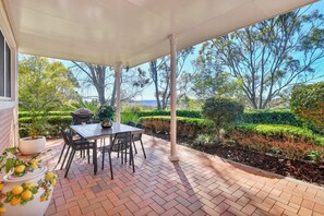 A covered patio with a table and chairs, surrounded by a landscaped garden and trees.