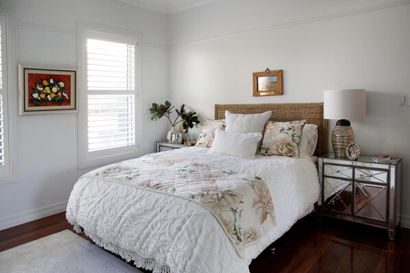 Une chambre à coucher avec un grand lit, une table de chevet avec une lampe, un tableau encadré et une fenêtre avec des stores.