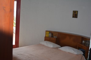 Ein Schlafzimmer mit einem Bett, Kissen, einem Nachttisch mit Büchern, einem kleinen Tisch mit einer Lampe und einem Wandbild.