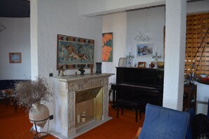 Ein Zimmer mit Kamin, Klavier und verschiedenen Kunstwerken an den Wänden.