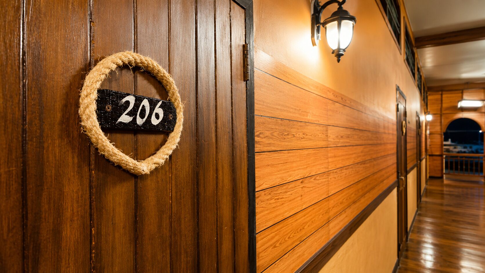 Un pasillo de madera con un cartel con el número 206 y una lámpara fijada a la pared.