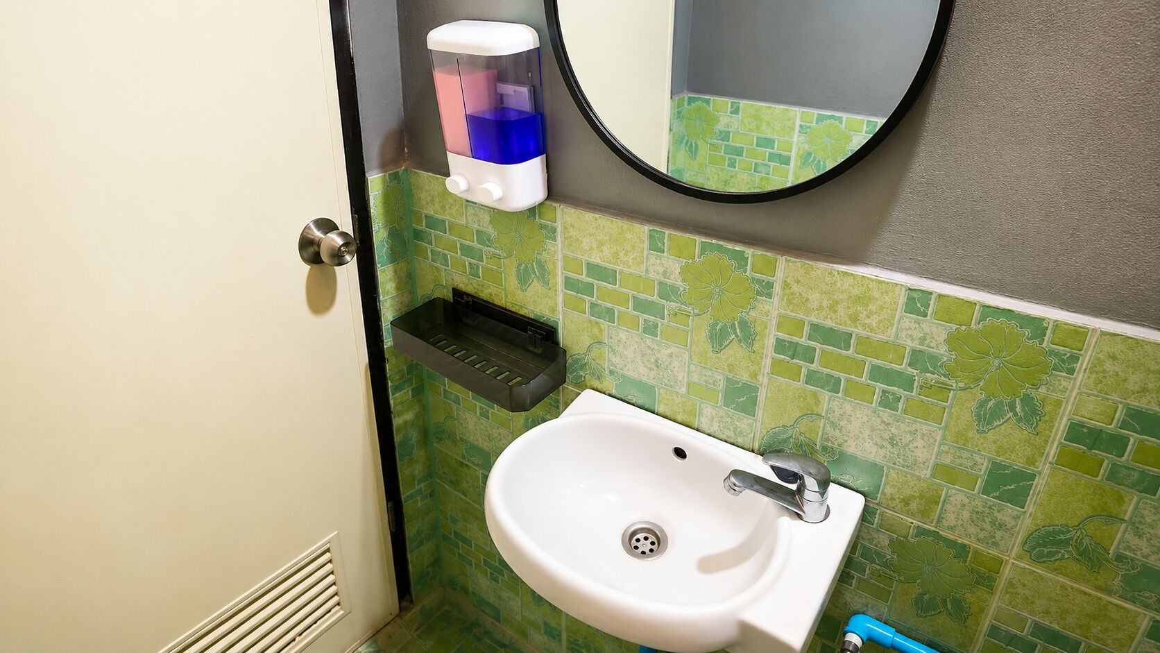 A bathroom with a white sink, a mirror, and a soap dispenser.
