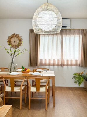 Ein Essbereich mit einem Holztisch, Stühlen, einer gewebten Pendelleuchte, einer Wanduhr und einem Fenster mit Vorhängen.
