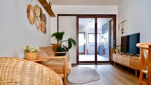 Ein Wohnzimmer mit einer Couch, einem Fernseher, einem Holzschrank und einem großen Fenster.