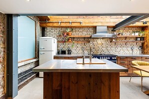A kitchen with a brick wall, wooden shelves, a stainless steel sink, and a stove. - 2 Bed Garden Retreat by Victoria Park (London)