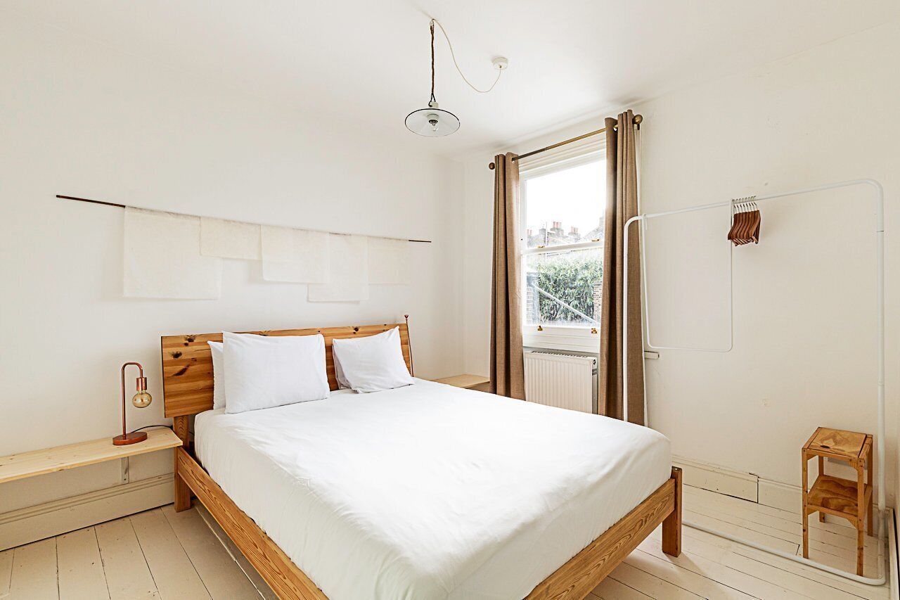 A bedroom with a wooden bed, a nightstand, a bedside lamp, a window with curtains, and a radiator.