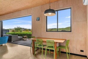 Ein modernes Interieur mit Holzboden, großen Fenstern, einem Esstisch mit Stühlen und einem blauen Sessel.