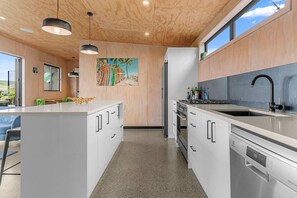 A modern kitchen with a central island, stainless steel appliances, and a wooden ceiling. - Hidden Treasure in Mangawhai Village + EV charger (Mangawhai)