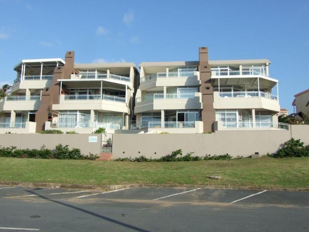 A multi-story residential building with balconies, a parking lot, and a clear sky.