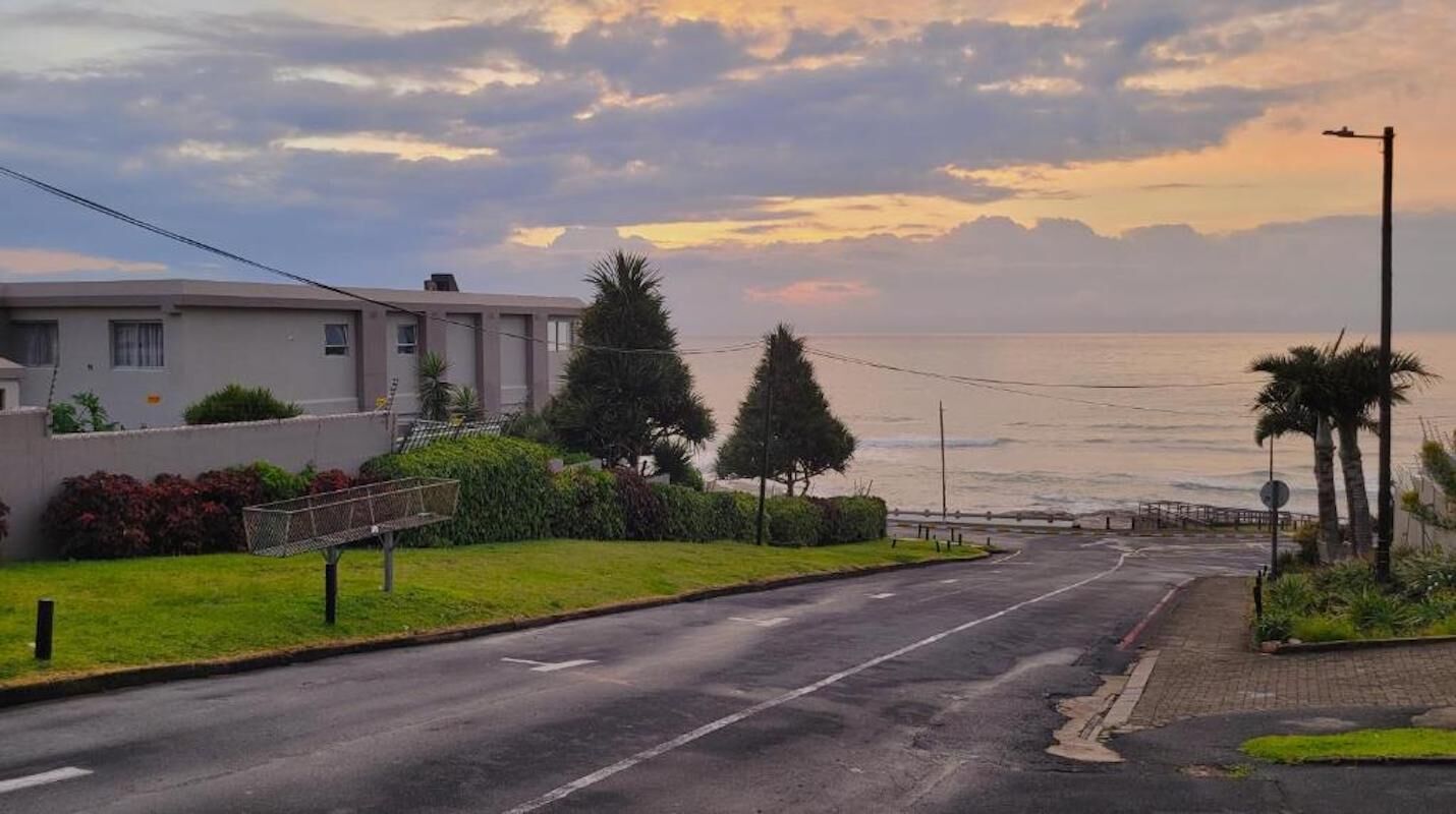 A coastal street with a building, a sidewalk, and a view of the sea.