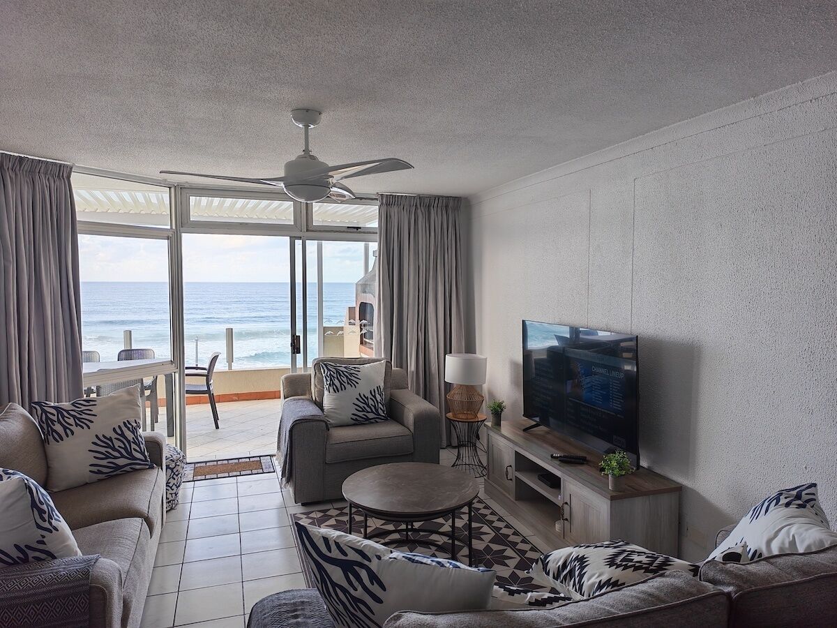 A living room with a TV, sofa, and a view of the ocean.