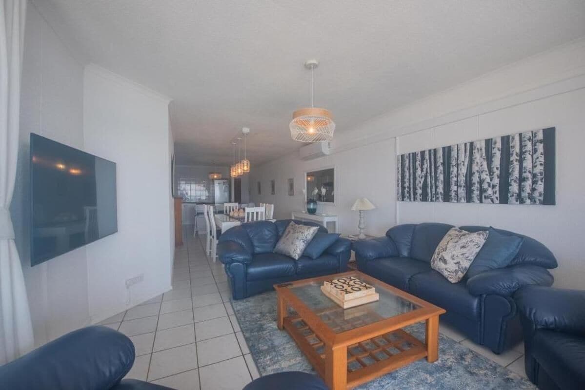 A modern living room with blue leather sofas, a wooden coffee table, and a large painting on the wall.