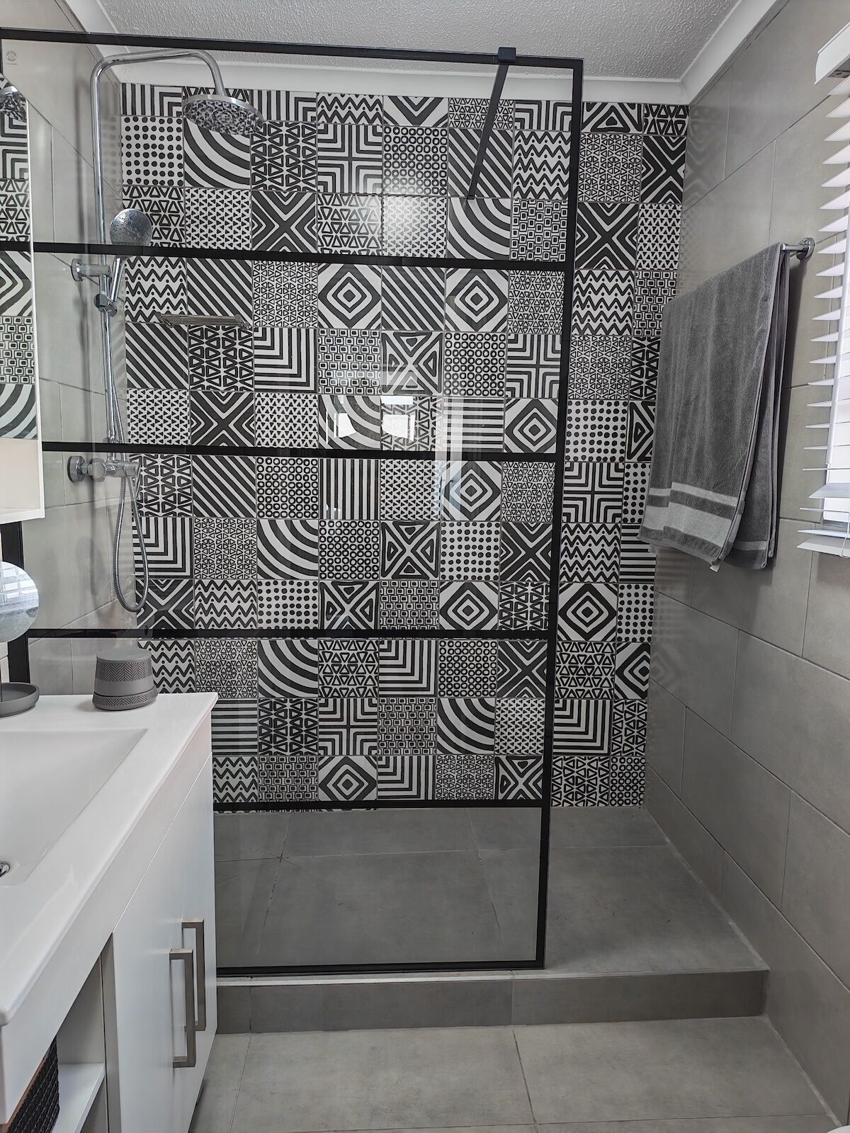 A bathroom with a shower area featuring geometric patterned tiles, a glass shower enclosure, and a white sink with a mirror.