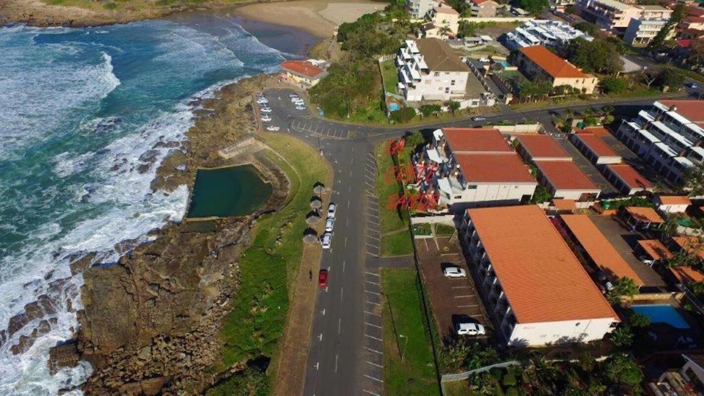 Vista aérea de una zona costera con una carretera que lleva a una playa, edificios residenciales y un estacionamiento.