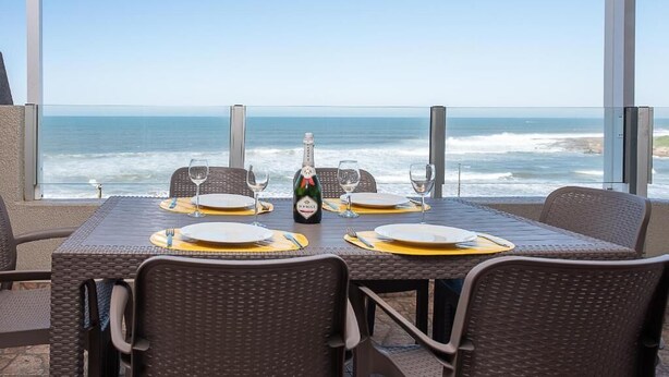 A table set for four with a bottle of champagne, facing a view of the ocean.