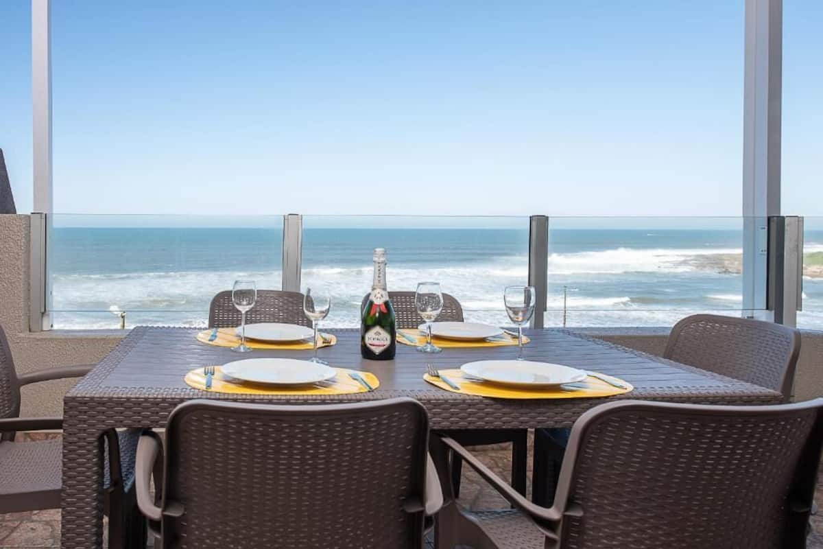 Une table dressée pour quatre personnes, avec une bouteille de champagne, donnant sur une vue imprenable sur l’océan.