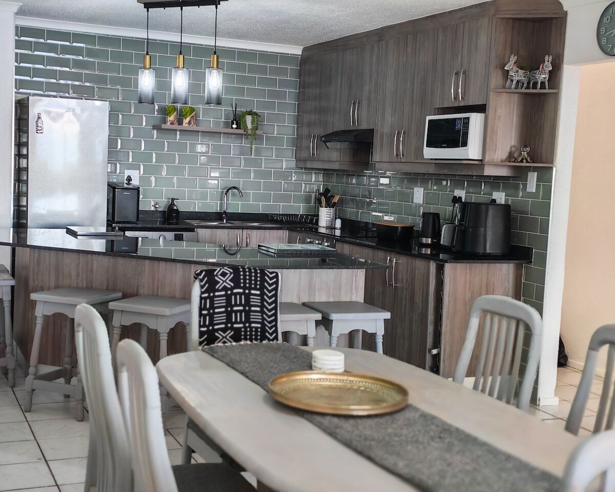 Eine moderne Küche mit Einbauherd, Mikrowelle und einem großen Kühlschrank. Es gibt eine Bar mit Barhocker und einen Esstisch mit gemustertem Tischläufer.