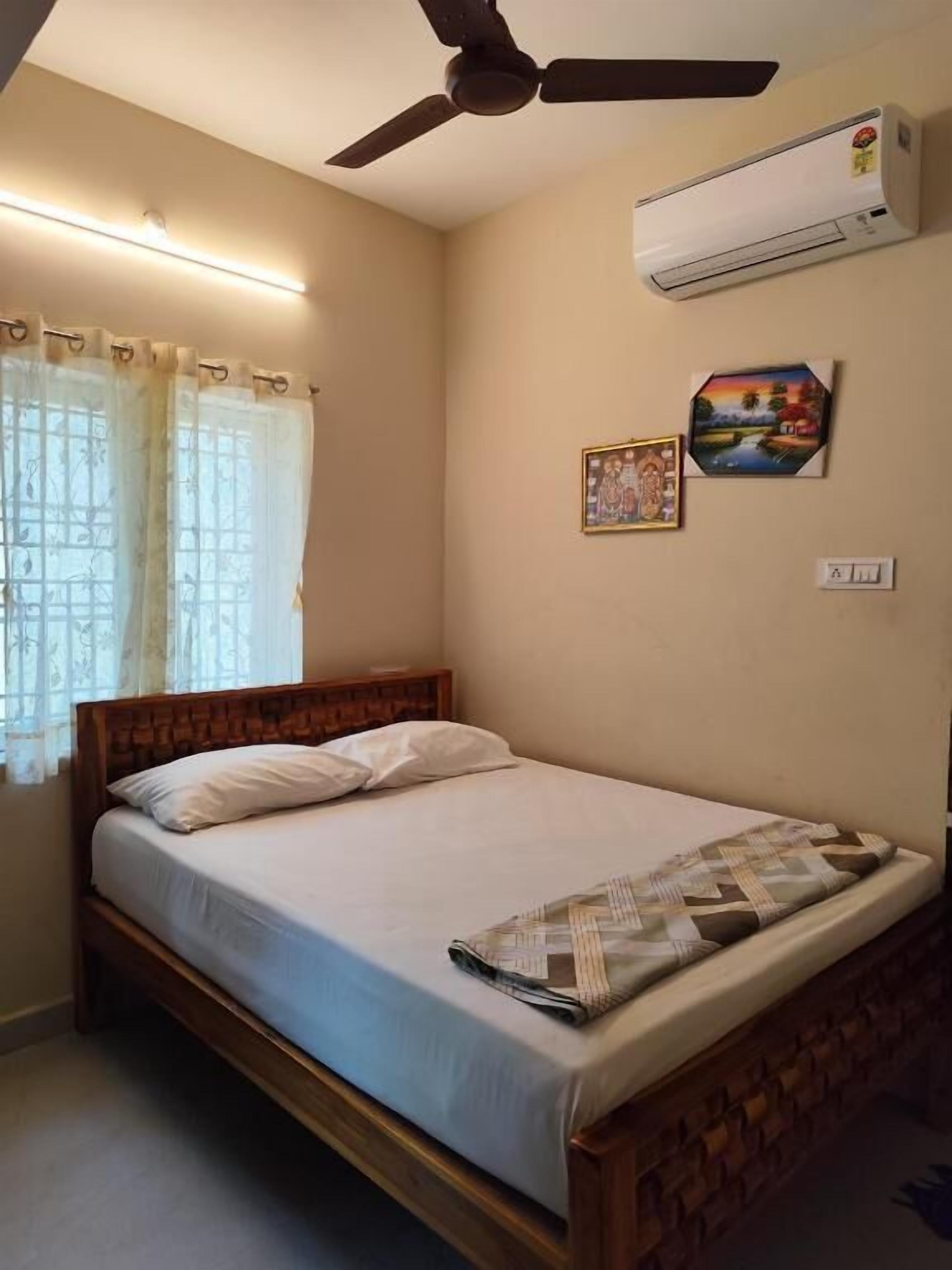 A bedroom with a bed, a ceiling fan, an air conditioner, and a window with curtains.