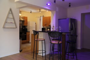 A modern kitchen with wooden cabinets, a stainless steel refrigerator, and two bar stools. - Villa Oasis Provençale 3 étoiles avec piscine, jacuzzi, terrain de pétanque. (Cavalaire-sur-Mer)