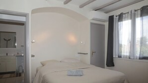 Un dormitori amb un llit, un bany amb un vàter i una finestra amb cortines.