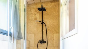 Une douche avec une porte en verre, un sol en bois et une serviette sur le sol.
