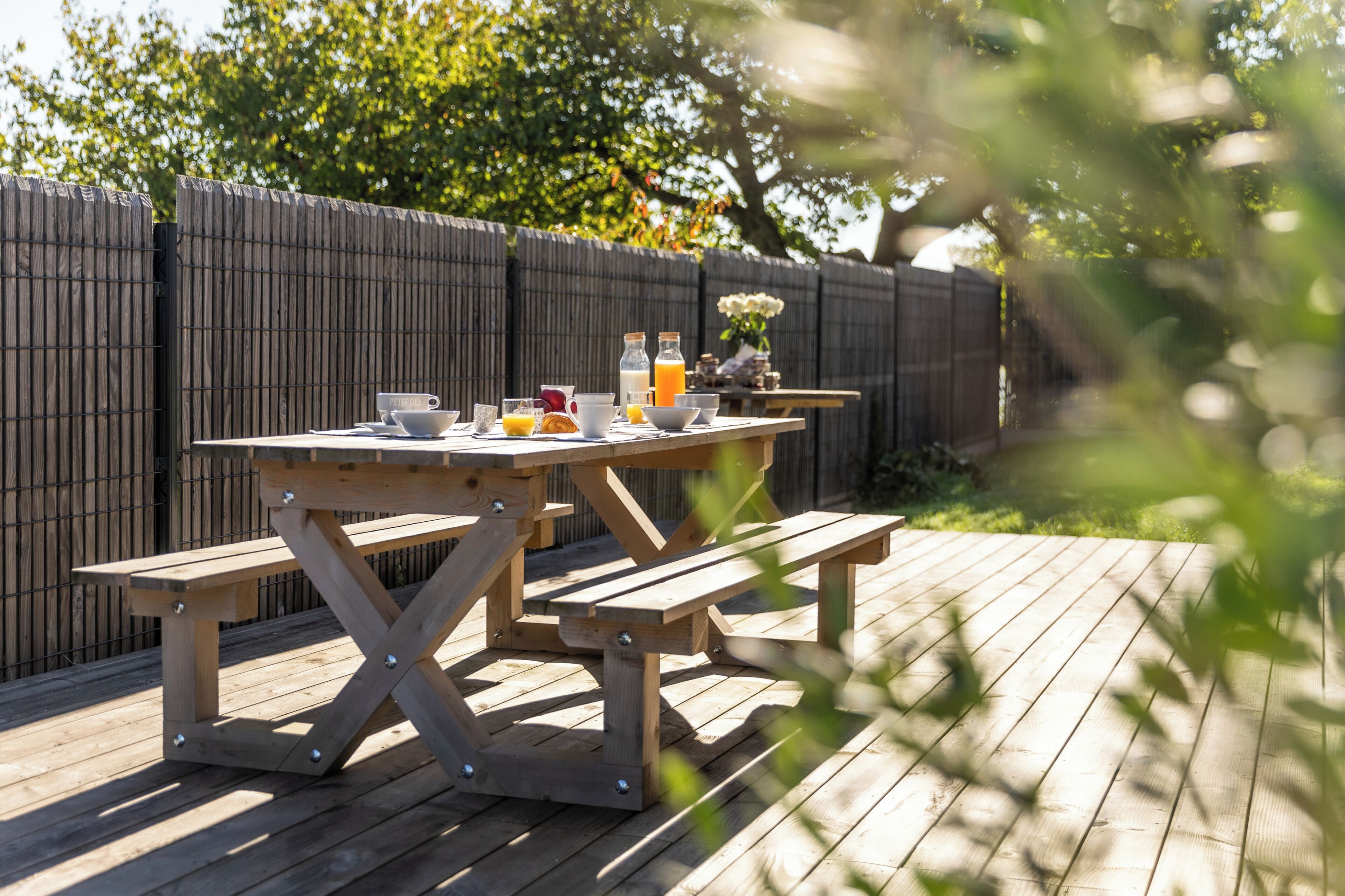 Une table de pique-nique en bois avec des bancs, une bouteille de jus de fruits et un saladier rempli de fruits.