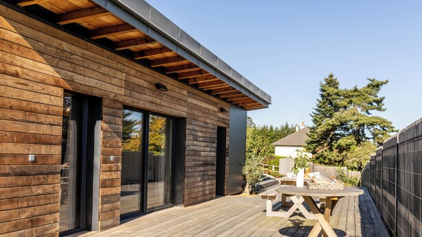 Une terrasse moderne en bois, avec une table et des chaises, une porte-fenêtre coulissante et une vue sur les environs.