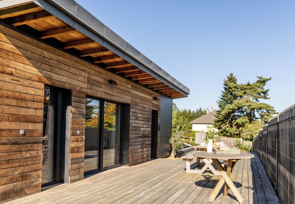 A modern wooden deck with a table and chairs, a sliding glass door, and a view of the surrounding area.