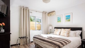 Un dormitorio con cama, cortinas, televisor, ventana y obras de arte en la pared.
