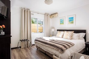 A bedroom with a bed, curtains, a TV, a window, and artwork on the wall. - Lu's Guest House your homely experience (Paarl)