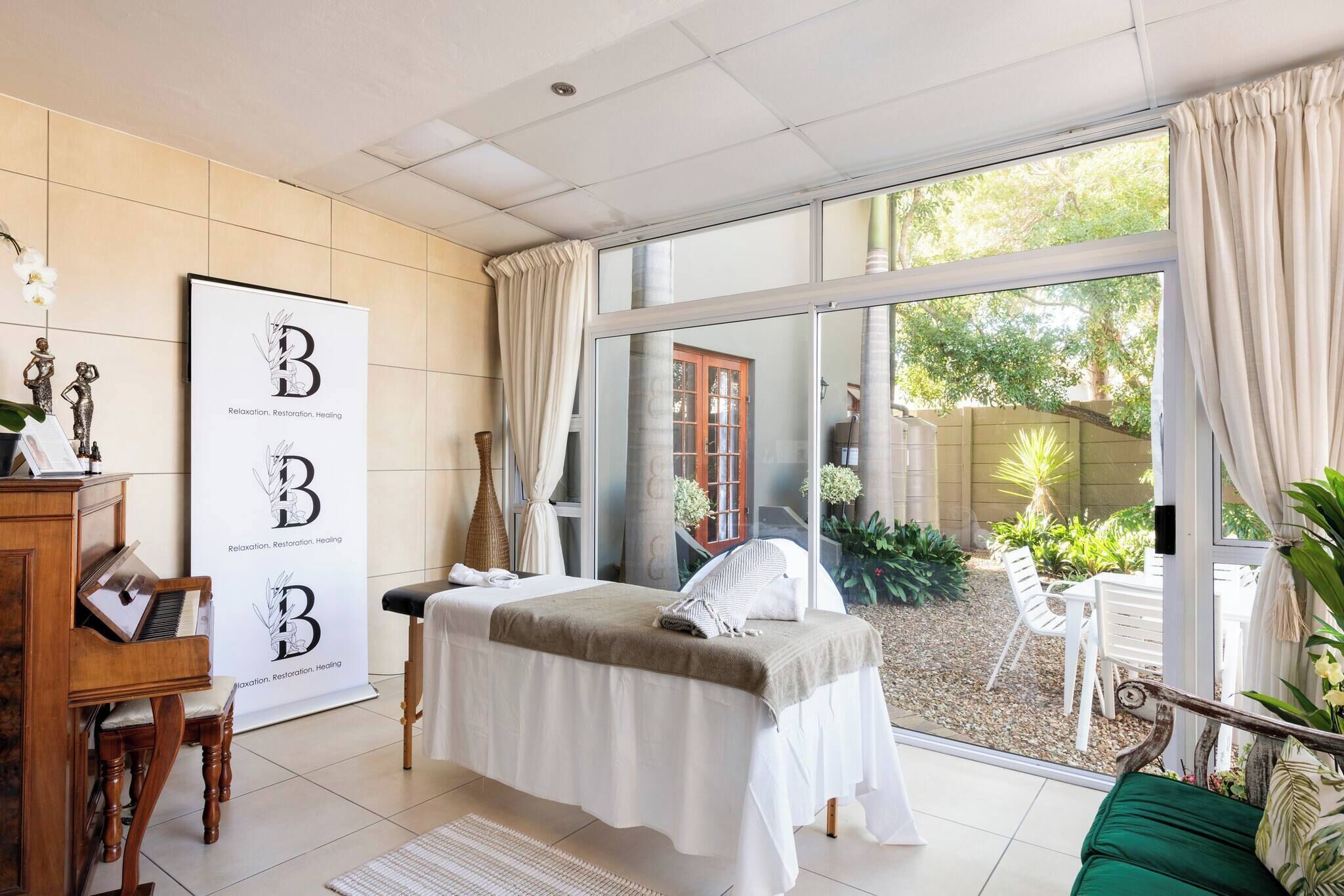 Een spa-ruimte met een massagetafel, een piano en een poster met de letters 'B' en de woorden 'Ontspanning, Vernieuwing, Genezing'.