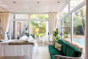 A room with a bed, a green sofa, and a view of a swimming pool and garden. - Lu's Guest House your homely experience (Paarl)