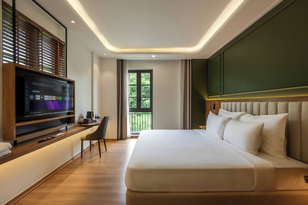 Habitación de hotel moderna con una cama grande, televisión de pantalla plana, escritorio y balcón con vistas a zonas verdes.