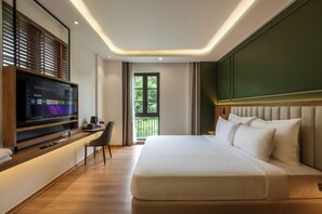 Habitación de hotel moderna con una cama grande, televisión de pantalla plana, escritorio y balcón con vistas a zonas verdes.
