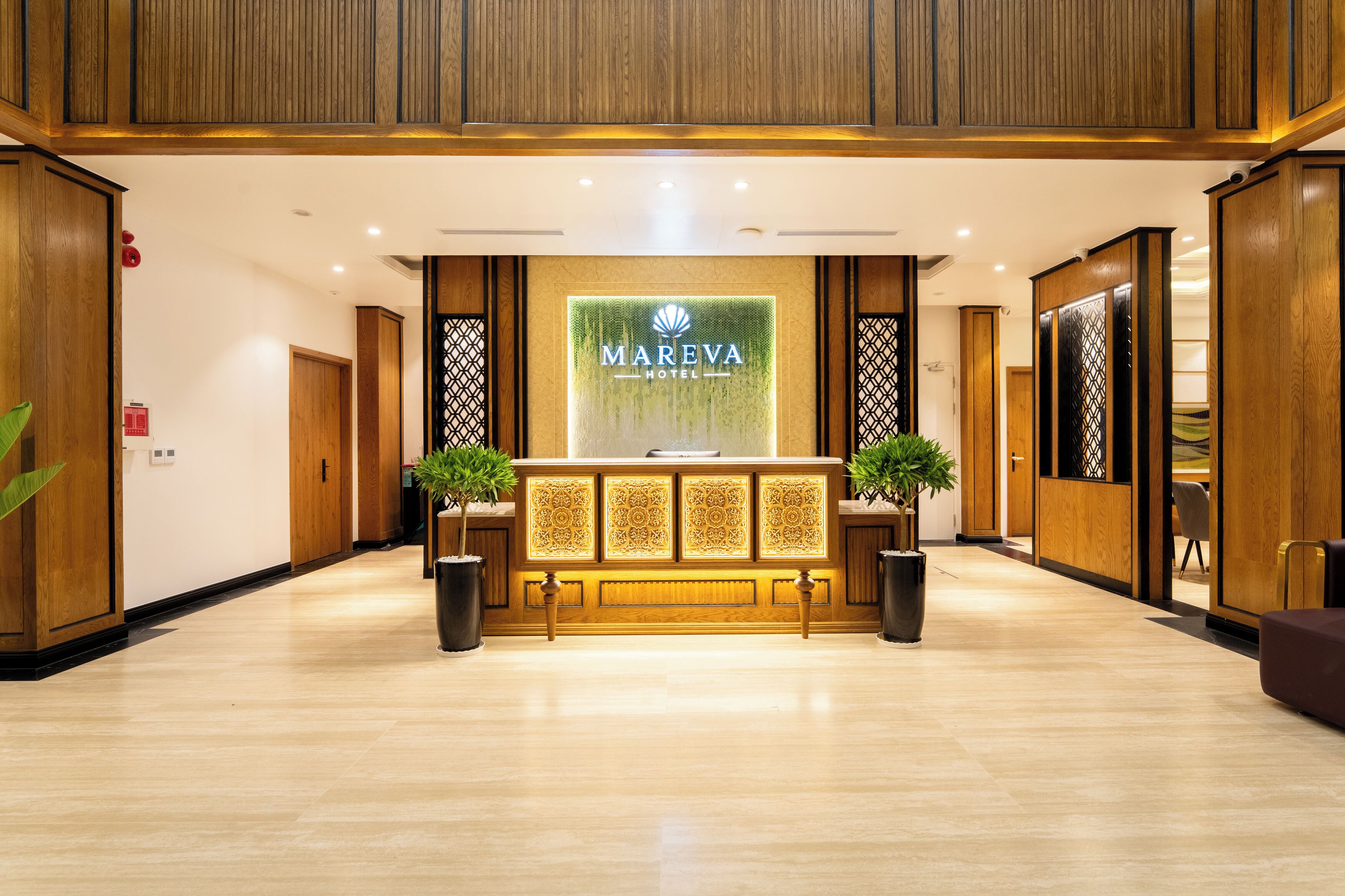 Zona de recepción de un hotel con un mostrador de madera, dos plantas en macetas y un gran letrero iluminado.