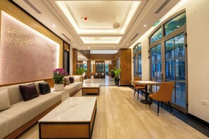 A hotel lobby with a seating area, a reception desk, and large windows.