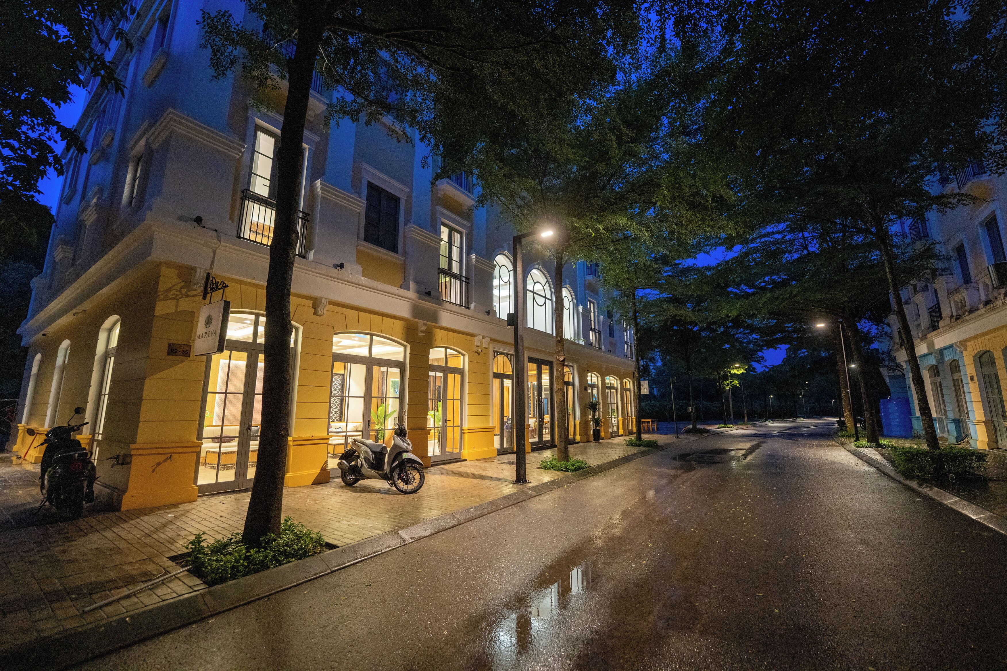 A street view at night with a building featuring large windows and a parked scooter.