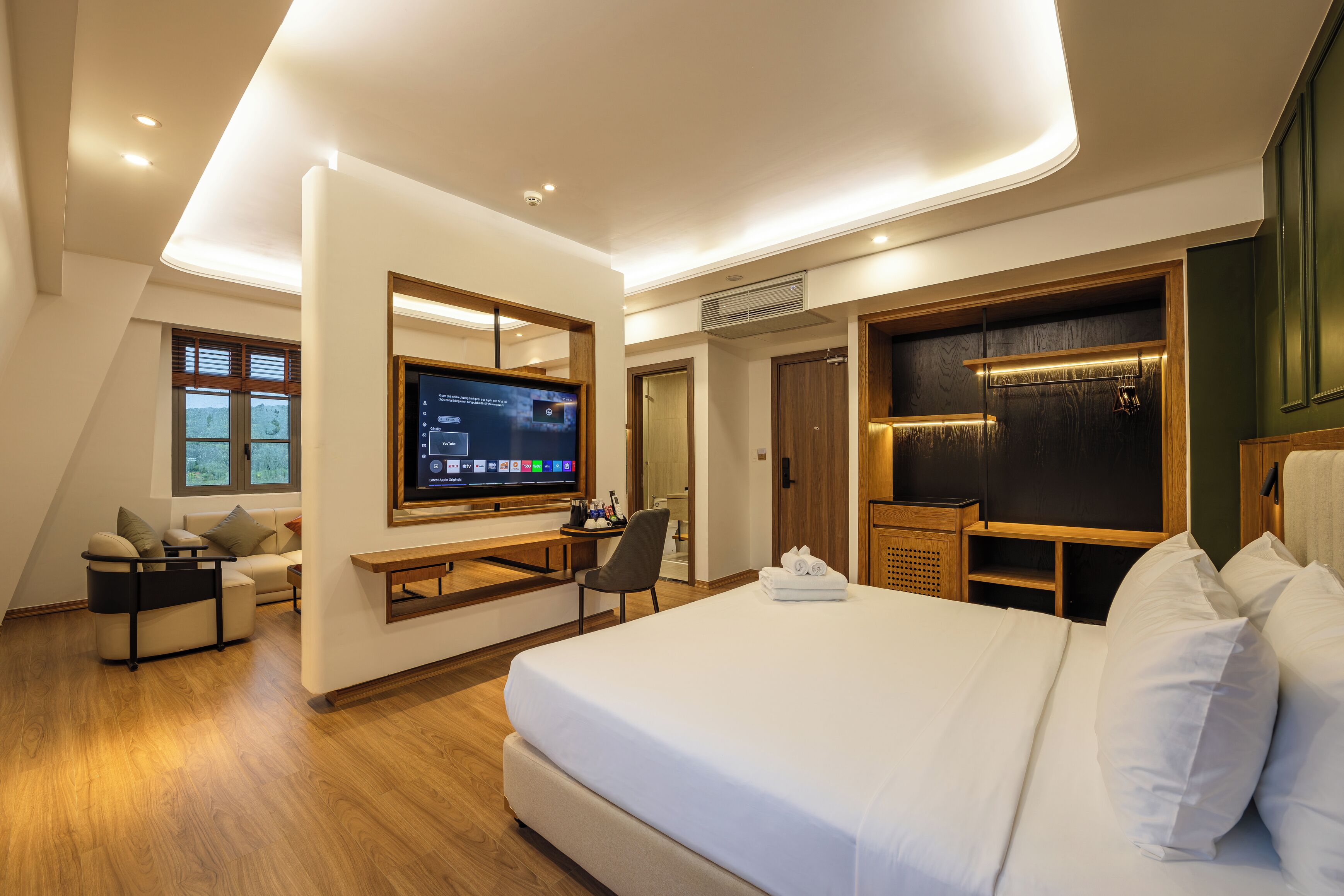 Habitación de hotel moderna con una cama grande, un escritorio, un televisor de pantalla plana y una zona de estar con vistas al exterior.