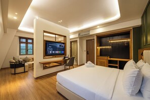 A modern hotel room with a large bed, a desk, a flat-screen TV, and a seating area with a view of the outdoors.