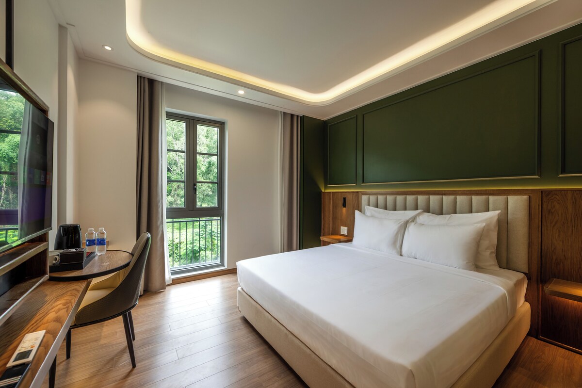 Habitación de hotel con cama, escritorio, silla, televisor y ventana con vistas a zonas verdes.