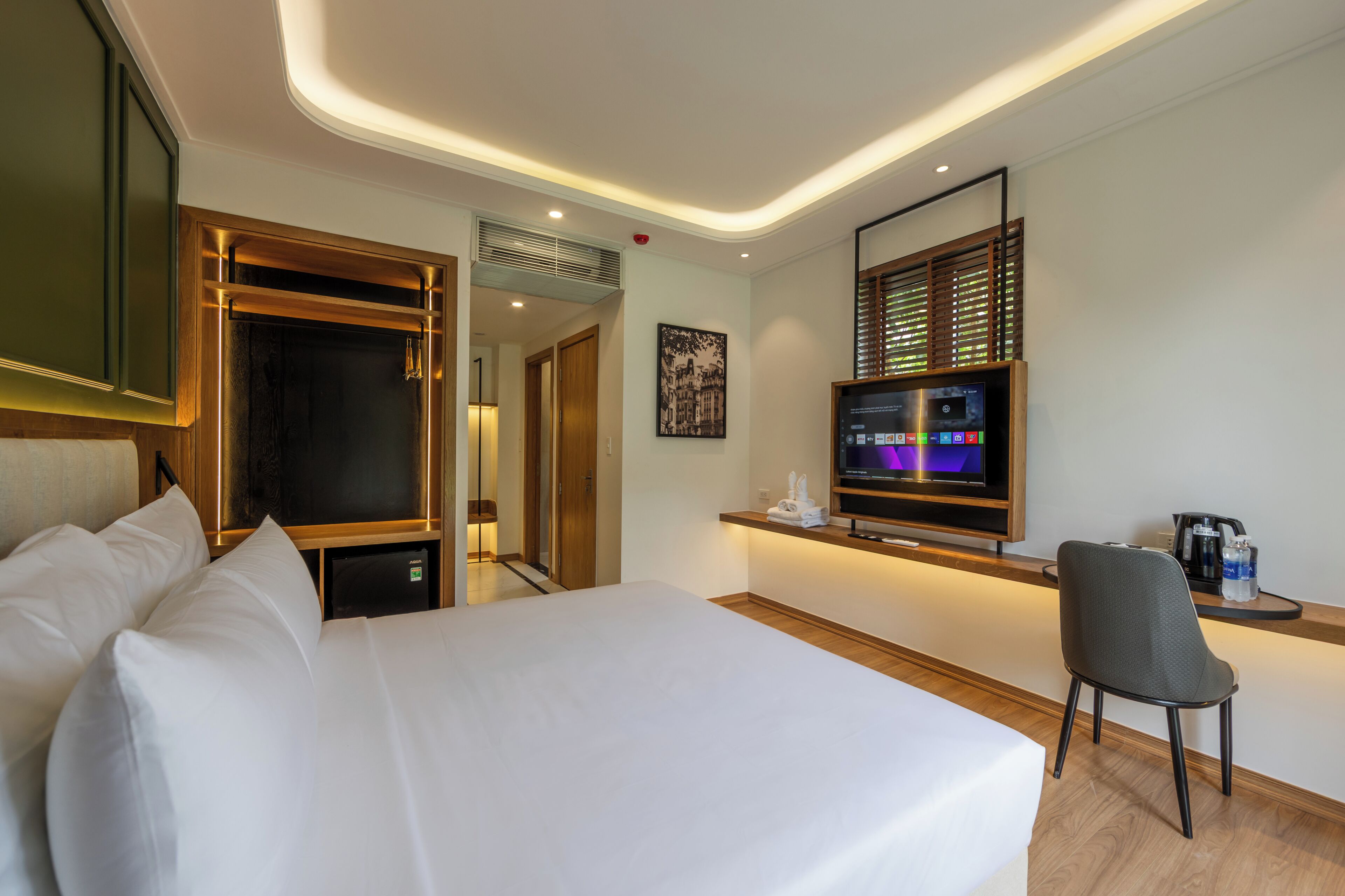 Una habitación de hotel con cama, un escritorio con silla, televisor y un cuadro en la pared.