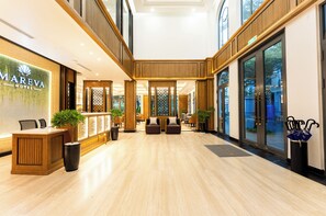 Vestíbulo de hotel con mostrador de recepción, zona de estar y ventanas amplias.