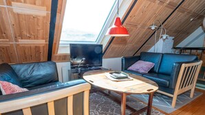 A loft-style room with a wooden ceiling, a black leather sofa, a blue sofa, a wooden coffee table, and a red pendant light. - 10 Person Holiday Home in Harboore (Harboore)