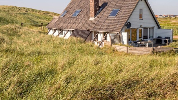 A white house with a sloped roof, a chimney, and a small porch with outdoor seating. - 10 Person Holiday Home in Harboore (Harboore)