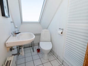 Ein kleines, weißes Badezimmer mit Oberlicht, Toilette, Waschbecken und Toilettenpapierhalter.